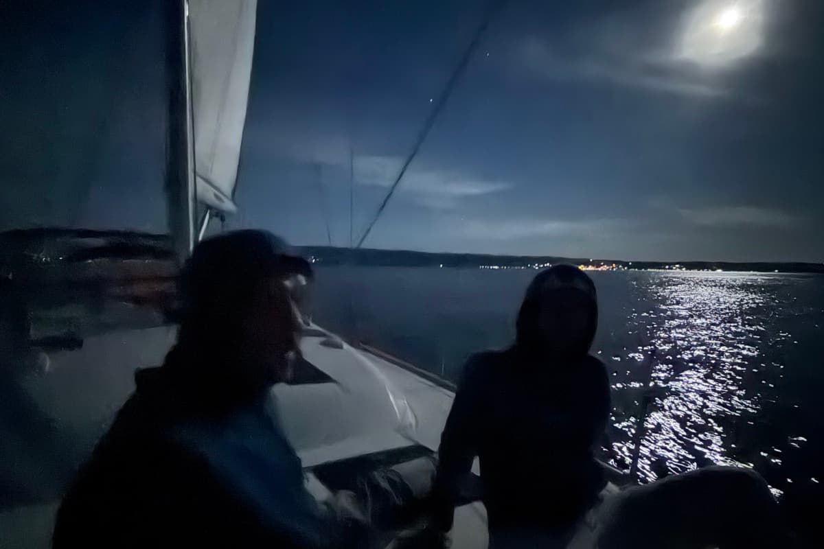 Zwei Männer an Deck beim Vollmondsegeln, der Mond spiegelt sich im Wasser