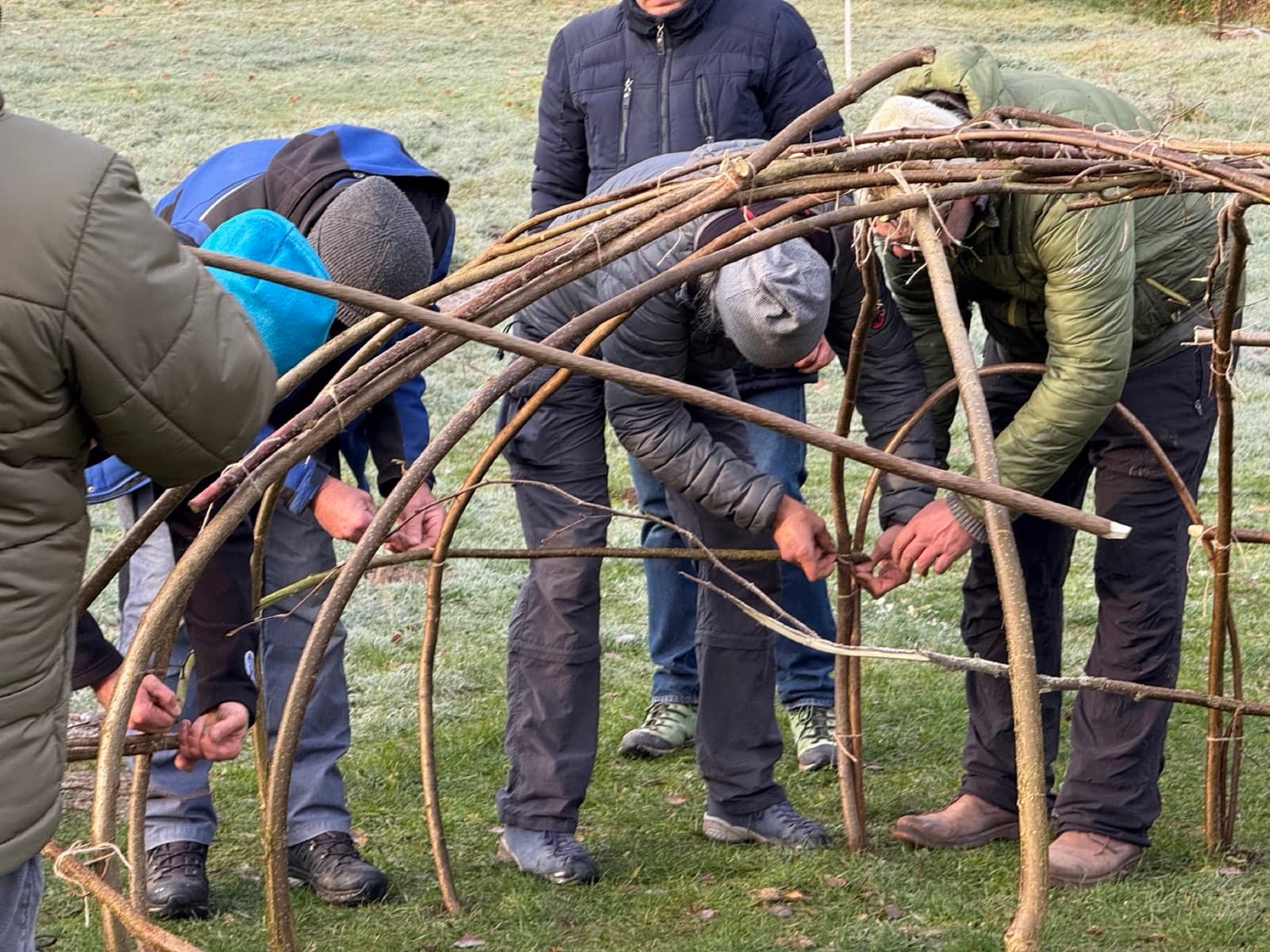 Männer biegen und verbinden Weidenruten zum Kuppelgerüst einer Schwitzhütte