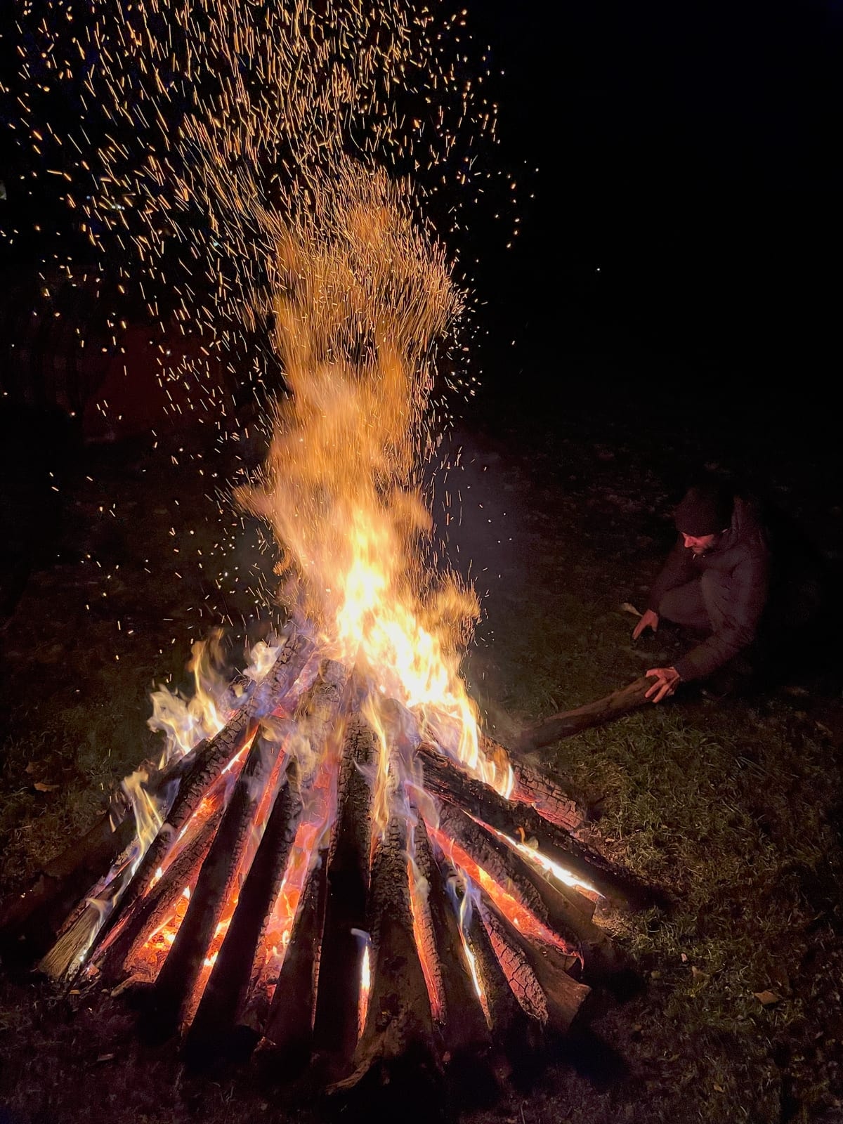 Ein Mann schürt mit einem Stock die Glut eines Lagerfeuers