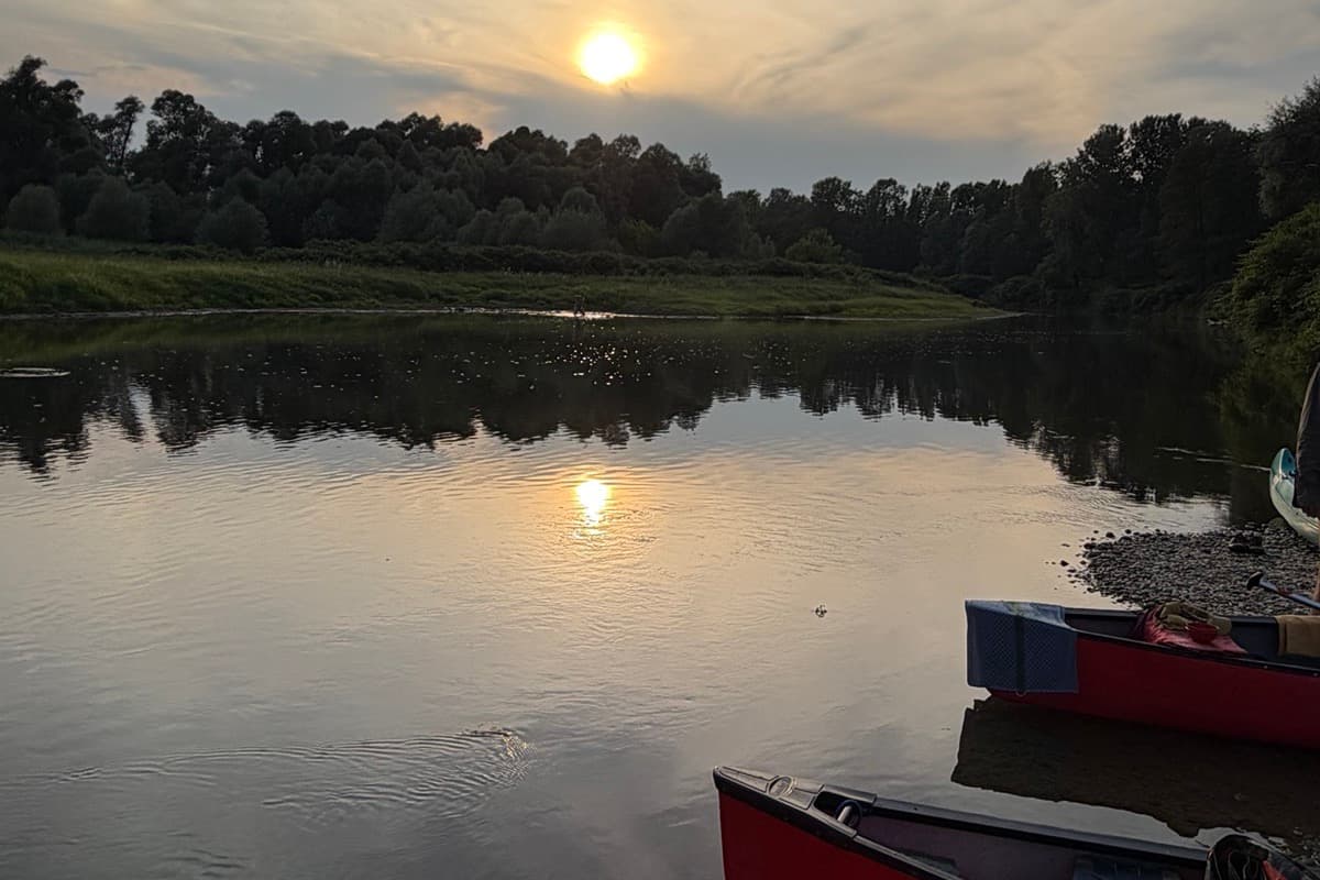 Sonnenuntergang über der Raab, im Vordergrund zwei rote Kanus am Ufer