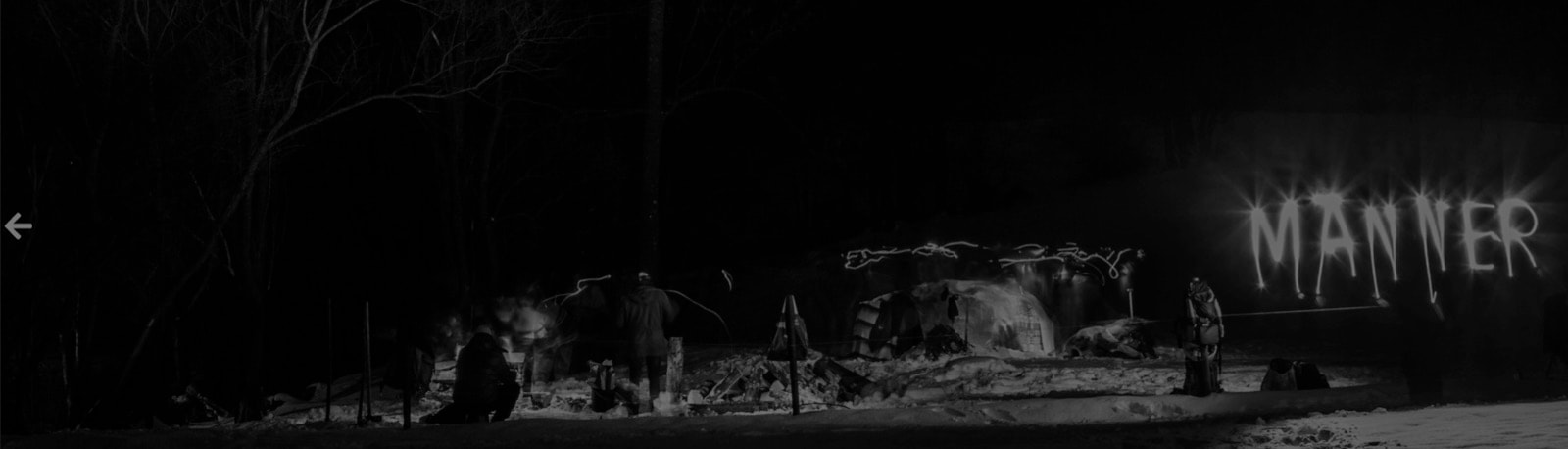 Nächtliches Winterlager im Schnee, im Hintergrund leuchtet das Wort „Männer“ in Lichtschrift